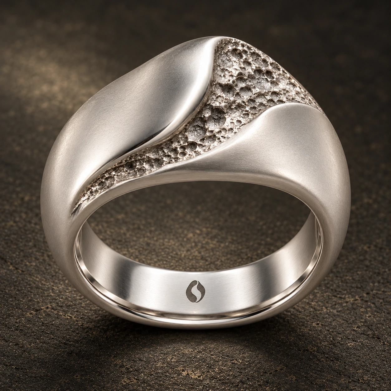 Concept de la bague Sillon : deux volumes argentés et fluides bordent une ouverture irrégulière à la texture minérale. Logo Ondralith gravé à l’intérieur.